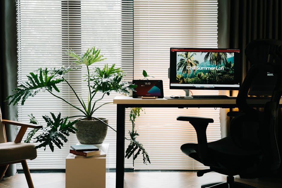 A stylish home office setup with a tropical plant, computer screen, and blinds enhancing summer vibes.