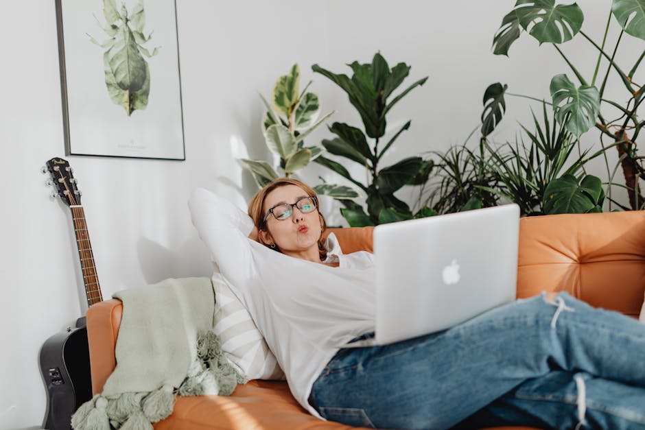 Woman lounging on a couch with a laptop, enjoying remote work from a stylish home setting.