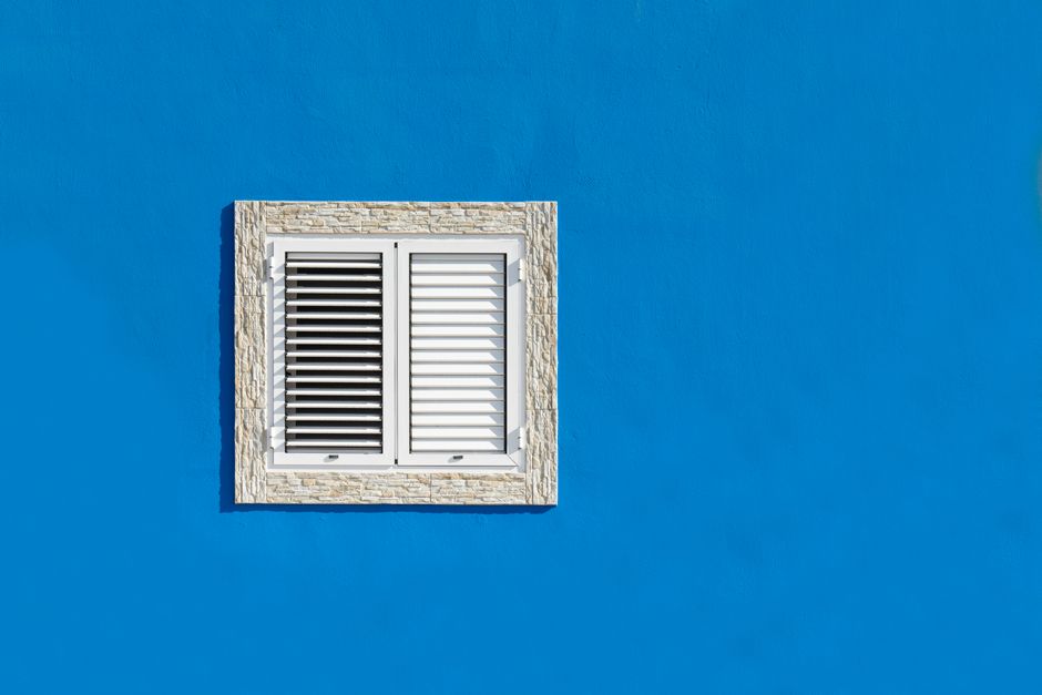 A striking minimalist image of a white stone-framed window on a vibrant blue wall.