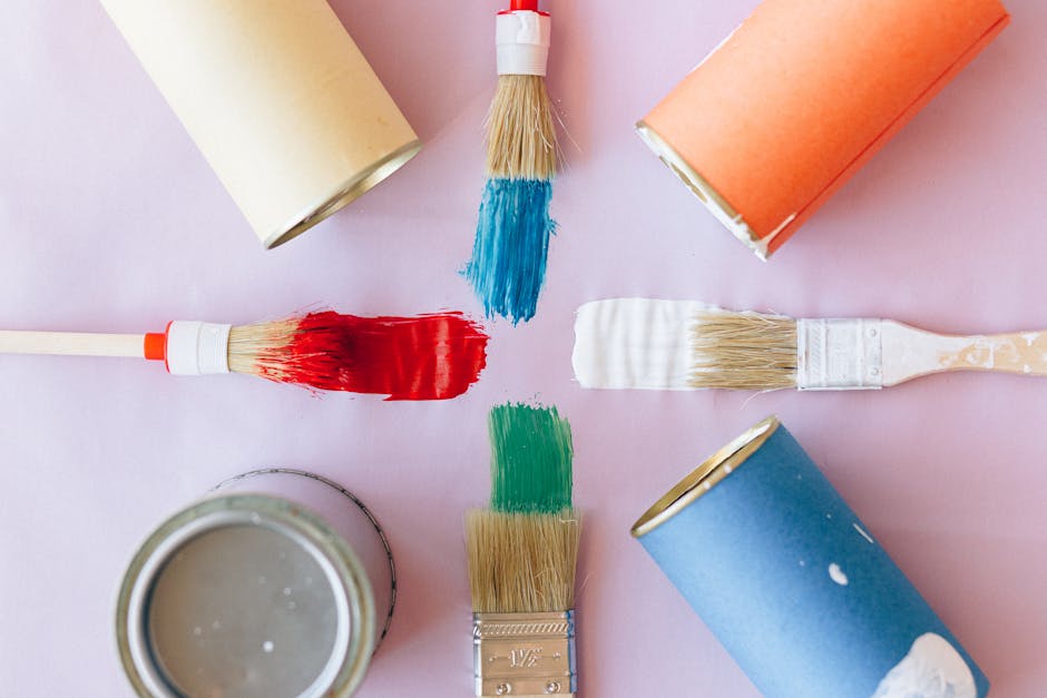 Top view of vibrant paintbrushes and cans against a pastel backdrop, ideal for creative projects.