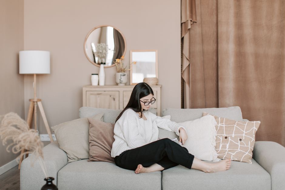 Young woman writing in notebook while sitting on a cozy sofa at home.