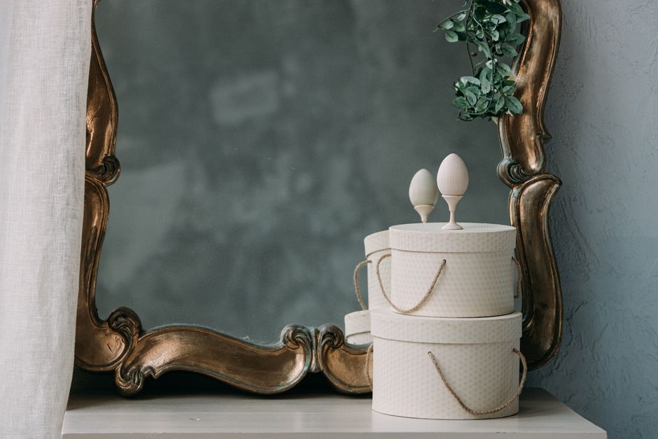 An elegant still life featuring an ornate mirror with decorative boxes and greenery, ideal for interior design concepts.