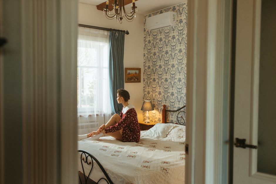 Adult sitting on a bed in a sunlit bedroom, exuding warmth and tranquility.