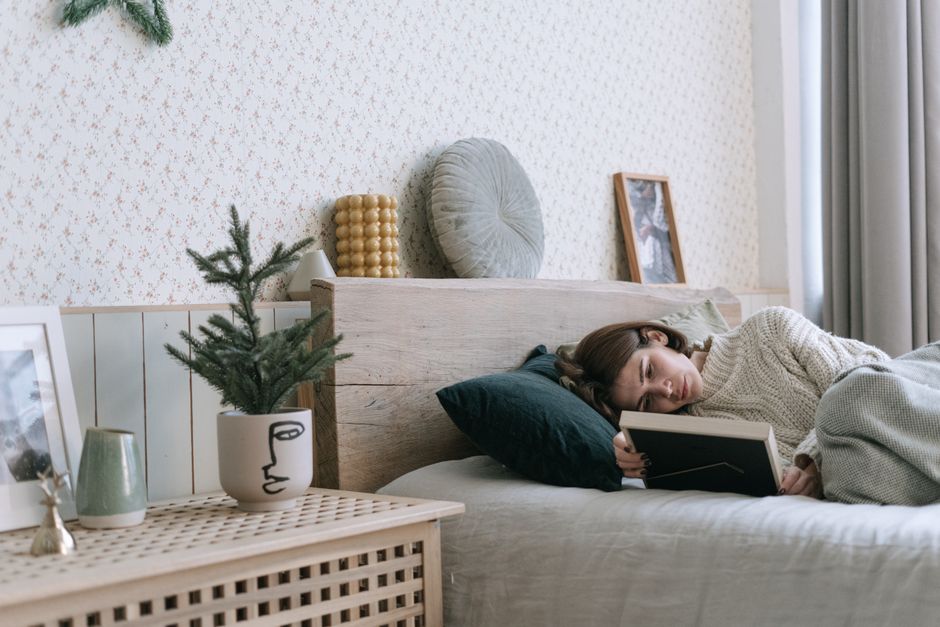 A woman in a cozy sweater lies on a bed, holding a picture frame, exuding a sense of longing and nostalgia.