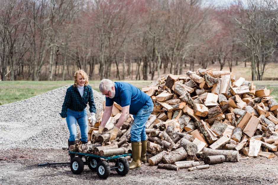 Mature couple working together to load chopped firewood onto a cart in a rural outdoor setting.