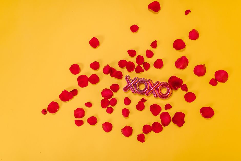 Red rose petals scattered with a XOXO sign on a vibrant yellow background.