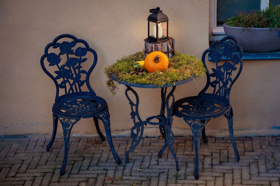 Charming outdoor fall setup with a pumpkin, lantern, and wrought iron furniture.
