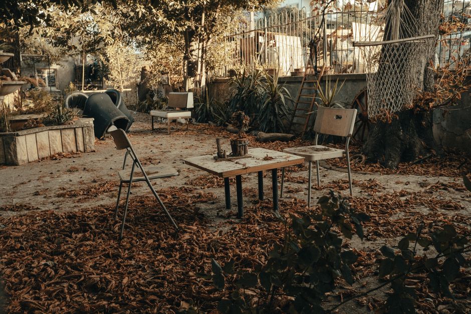 Weathered chairs and table in an abandoned garden setting, surrounded by fall leaves.