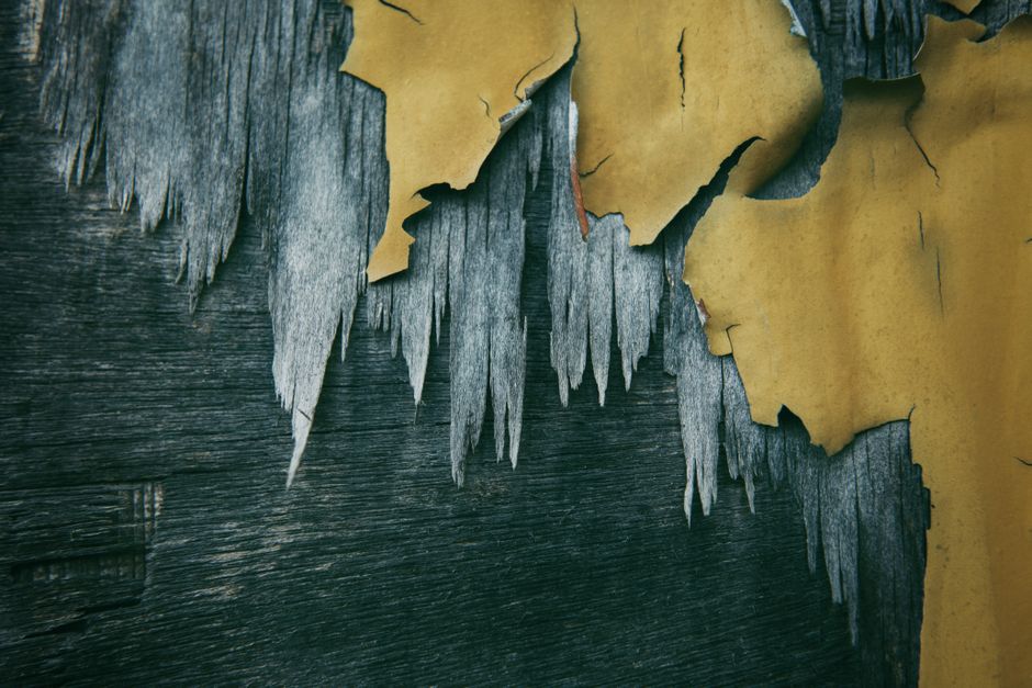 Close-up of a textured, peeling yellow and gray painted wooden wall, showcasing decay and color contrast.