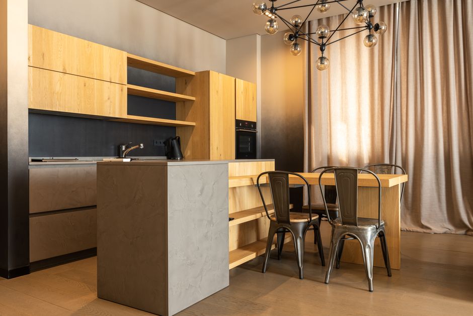 Table with chairs placed in spacious kitchen with wooden cabinets and appliances in stylish apartment with curtains on window at home