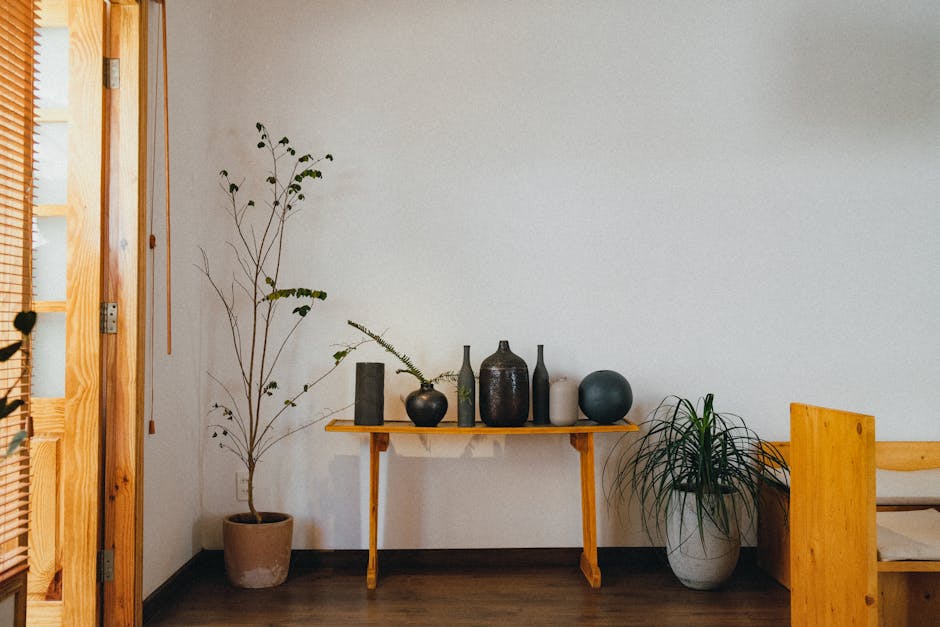 Serene minimalist interior featuring ceramics and potted plants on a wooden table against a white wall.
