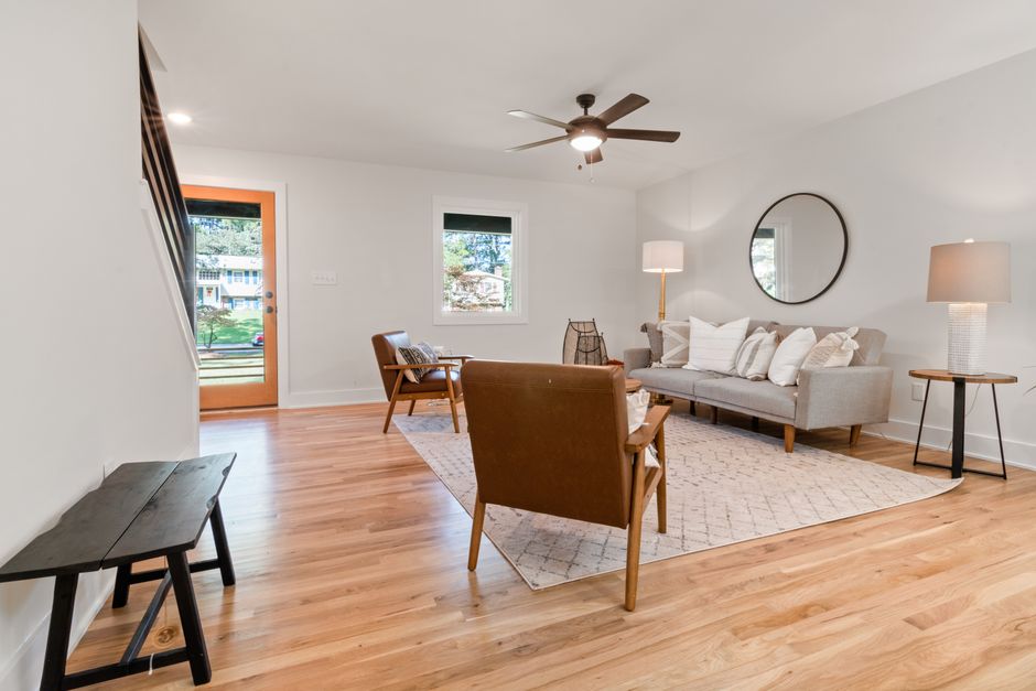 A contemporary living room featuring wooden flooring, a stylish sofa, and a ceiling fan for a relaxing ambiance.