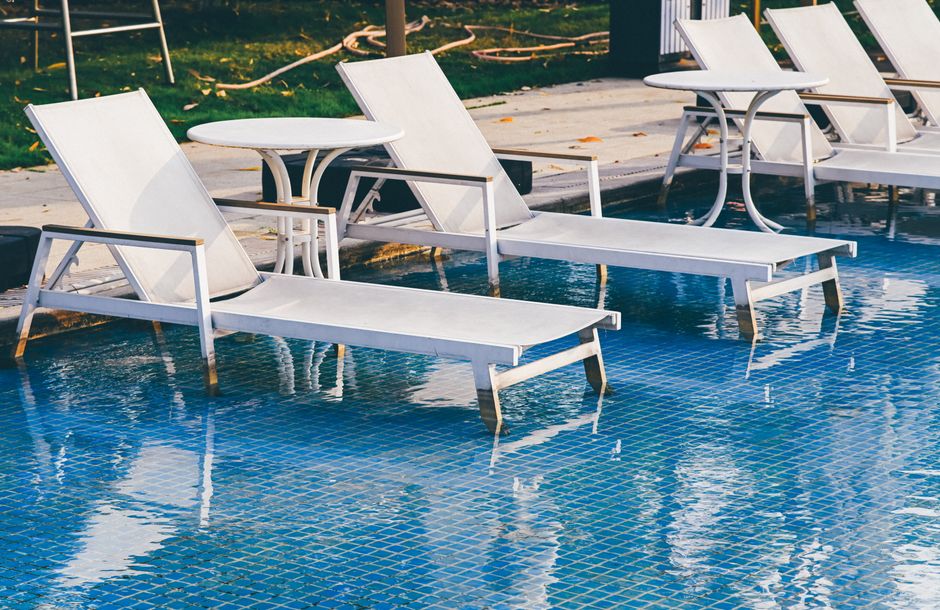 Chic white loungers and tables by a bright blue pool, perfect for relaxation.