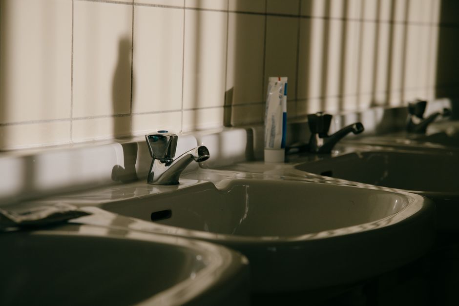 A row of bathroom sinks with faucets and shadows on tiled walls, creating a serene setting.