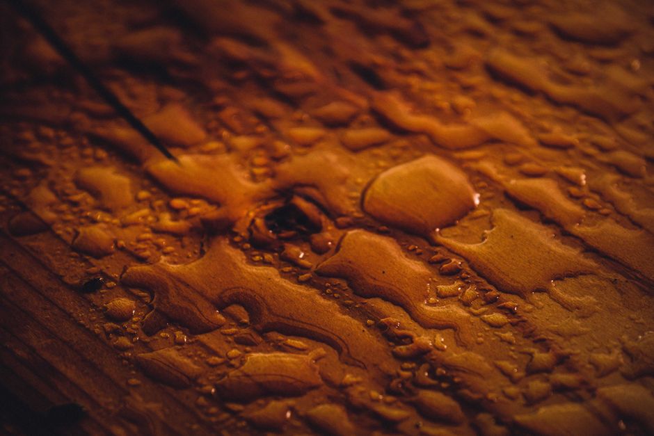 Selective focus of macro raindrops placed on brown wood surface with crack and knot