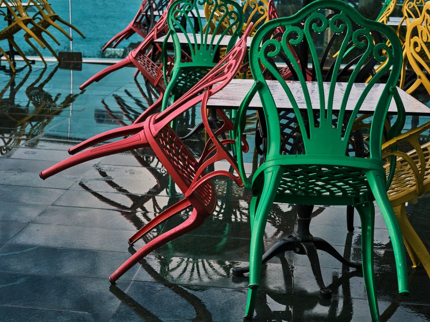 Vibrant red, green, and yellow metal chairs on a wet floor reflecting their lively colors.