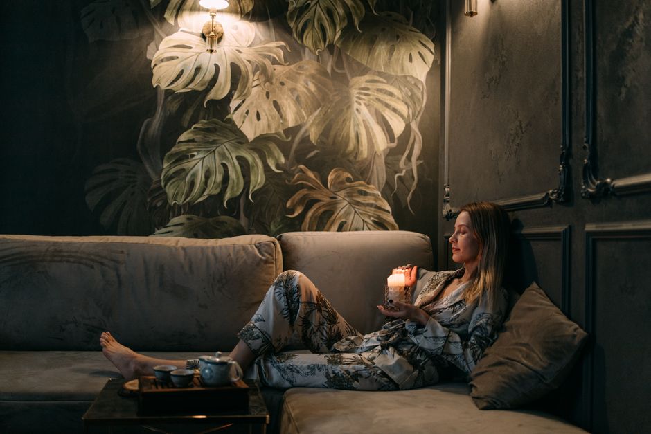 A woman relaxes on a sofa with a candle, creating a calming atmosphere indoors.