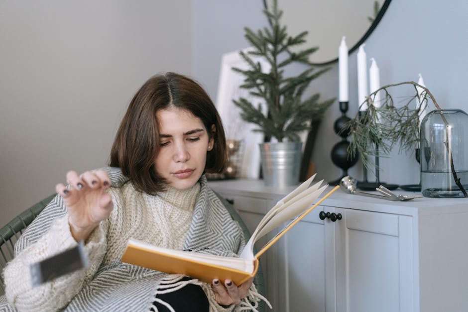 A woman in a knitted sweater enjoys reading a book at home, surrounded by cozy decor.