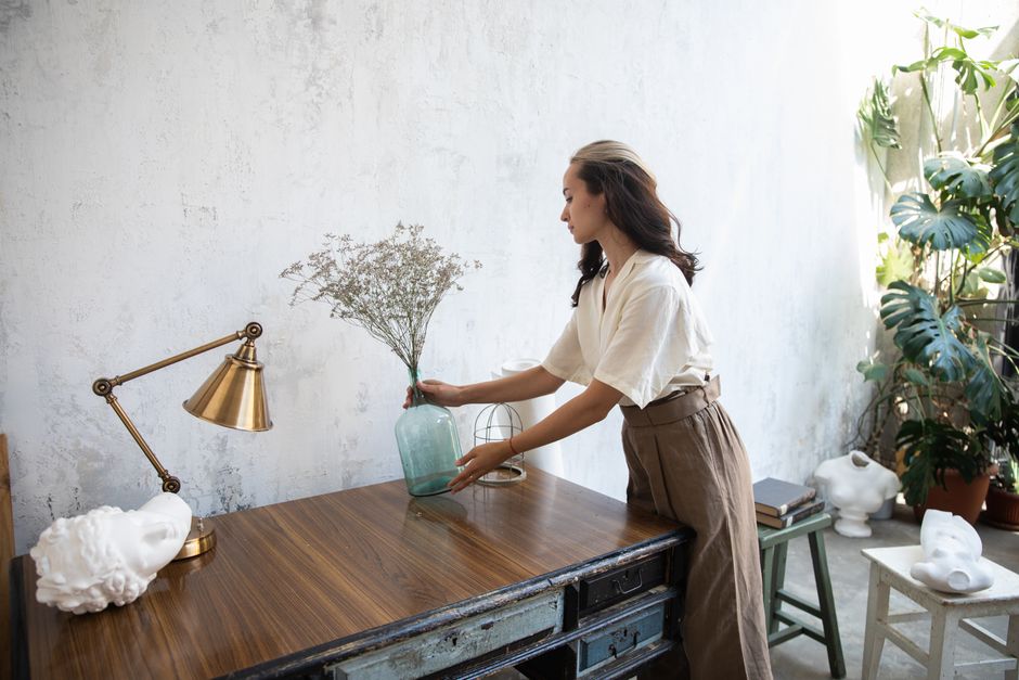 A woman arranging flowers in a stylish, artistic studio with natural lighting.