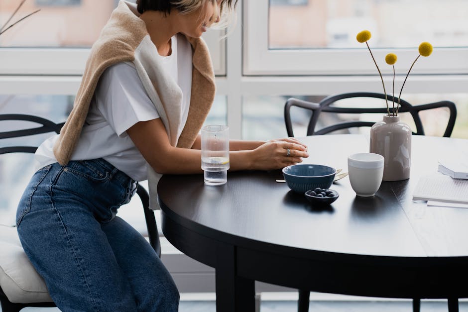 Woman in casual attire sitting indoors at a table with flowers and blueberries, creating a relaxed atmosphere.