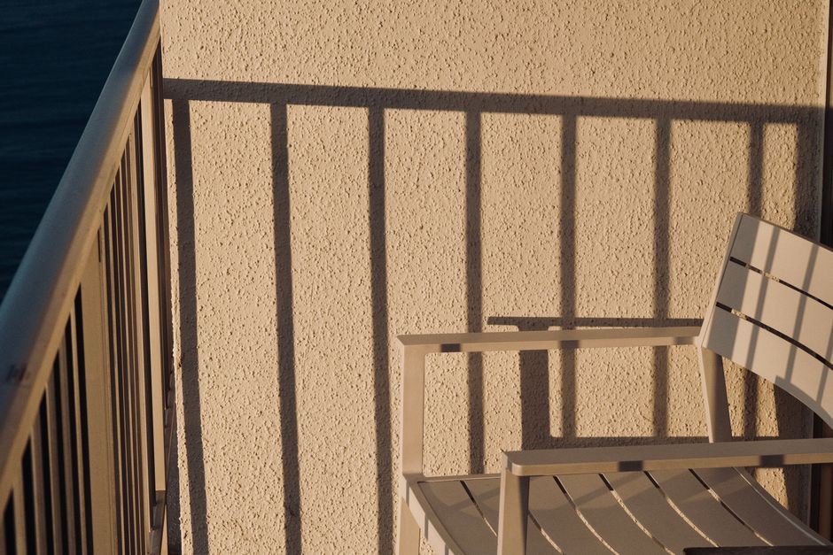 A serene balcony scene in Honolulu featuring shadows cast by the railing and a chair bathed in sunlight.