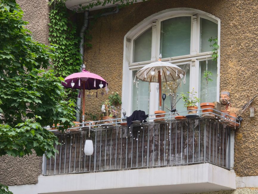 A quaint Berlin balcony decorated with plants and umbrellas, exuding urban charm.