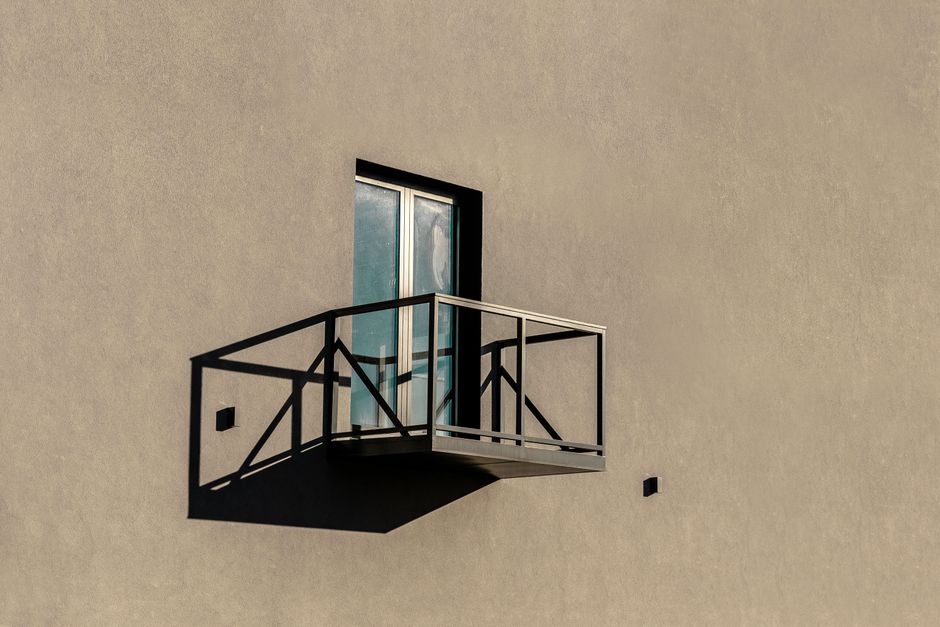 Simple exterior with a balcony casting a shadow in bright sunlight.