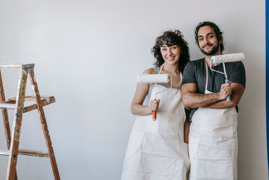 A cheerful couple with paint rollers ready for a home makeover, embodying creativity and teamwork.